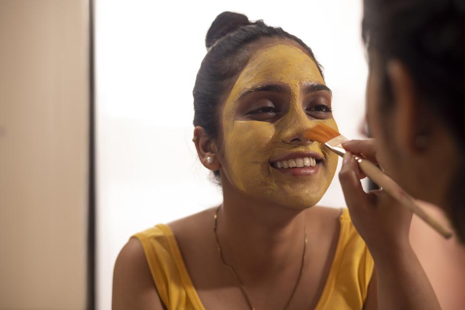 Woman applying a yellow face mask.