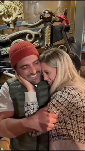 A man in a red beanie and a woman with blonde hair hugging and smiling.
