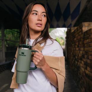 Woman holding a green Stanley tumbler with a straw.