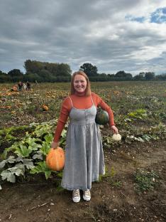 Woman in a pumpkin patch holding three pumpkins.