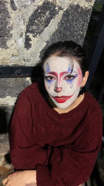 Woman in clown makeup wearing a maroon sweater.