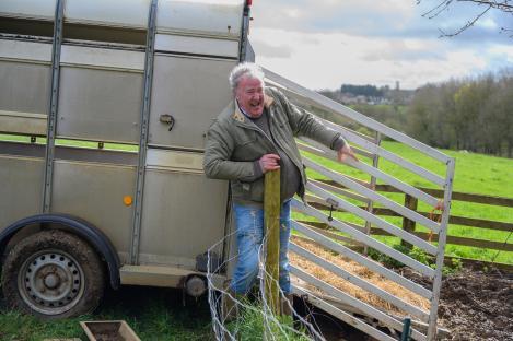 A laughing man leaning on a fence next to a livestock trailer.