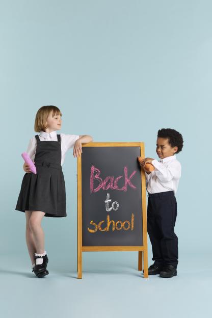 Two children in school uniforms stand on either side of a chalkboard that says