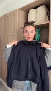 Woman holding up a black zip-up jacket.