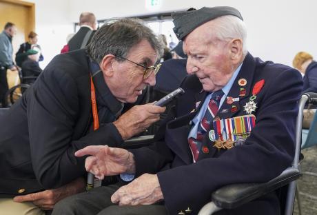 A reporter interviews a veteran in a wheelchair at a VE Day anniversary event.
