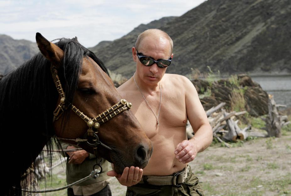 Russian Prime Minister Vladimir Putin, shirtless and wearing sunglasses, feeding a horse in Southern Siberia.