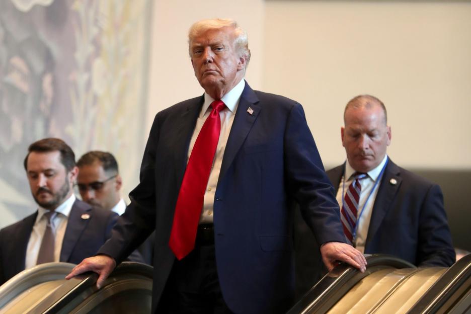 Donald Trump exiting the United Nations Headquarters, looking forward with security personnel behind him.