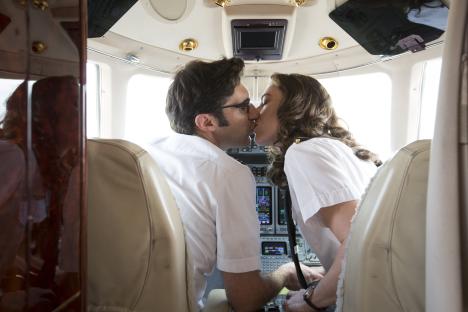Two pilots kissing in a cockpit.