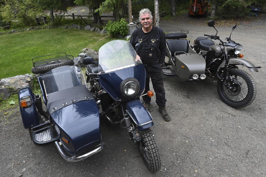 Man standing between two Ural motorcycles with sidecars.