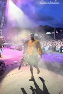 Man in yellow shirt carrying trophy on stage in front of a large crowd.