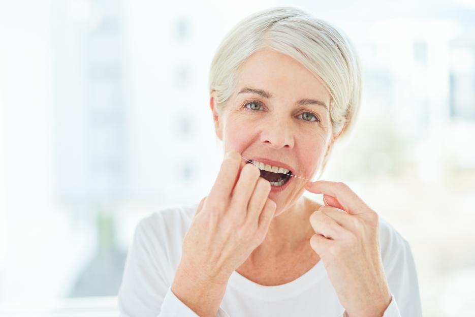 A mature woman with short gray hair flossing her teeth.