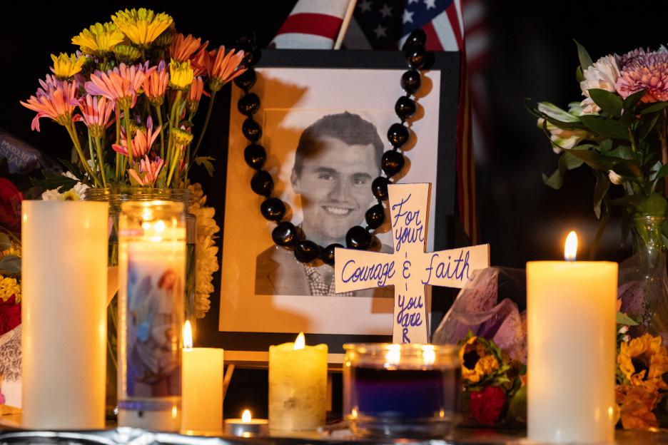 A memorial with candles, flowers, a framed photo of Charlie Kirk, and an American flag.