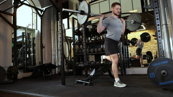 Man performing a barbell single-leg squat in a gym.