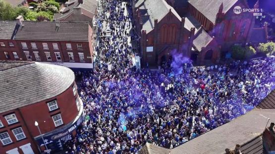 Aerial view of a large crowd of people in blue, many letting off blue smoke.