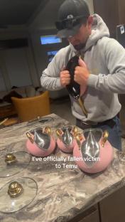 Man holding a frying pan, surrounded by pink pots and lids.