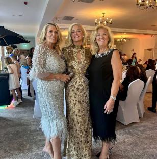 Three women in formal dresses at a wedding reception.