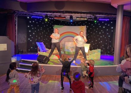 Two women performing on stage for children.