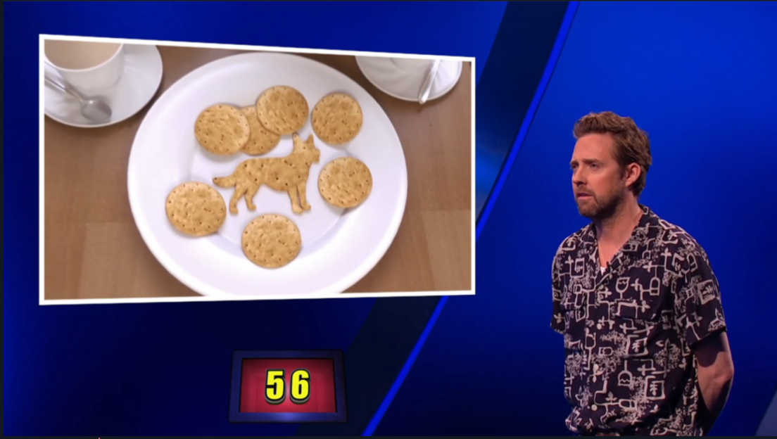 Screenshot of a game show contestant looking at a plate of crackers arranged in the shape of a dog.
