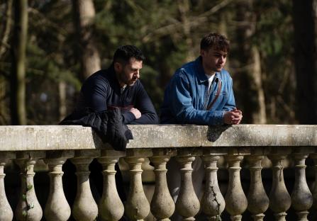 Two men leaning on a stone balustrade in a wooded area.
