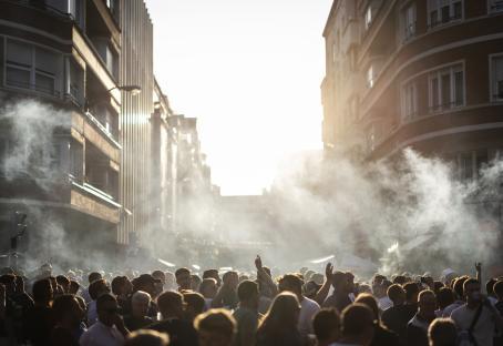 A crowd of people in a city street, with smoke or fog in the air.