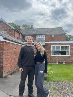 Couple standing in front of their brick house.