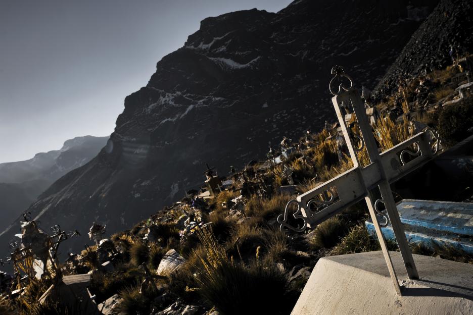 Cross atop a grave in a high-altitude cemetery, overlooking mountains.