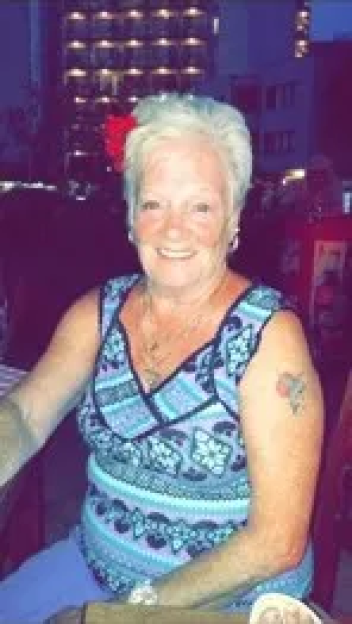 Woman in a blue patterned top smiling with a red flower in her white hair.