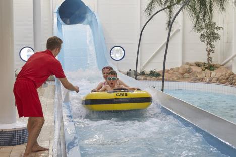Lifeguard watching children go down a water slide in a yellow tube.