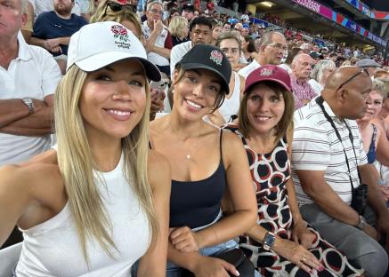 Three women wearing England rugby caps at a rugby match.