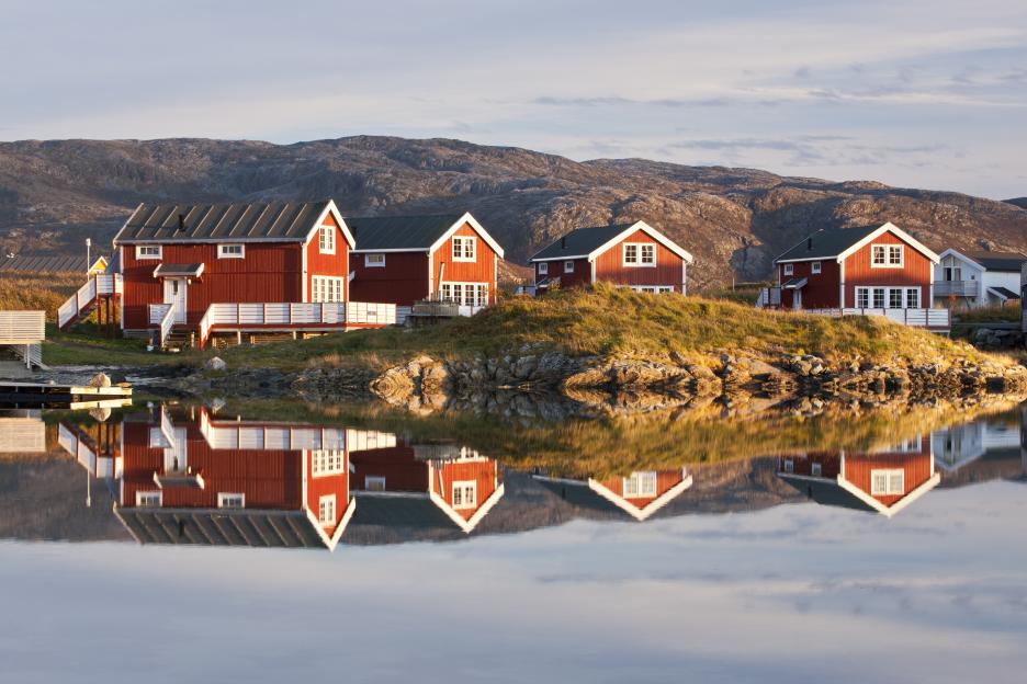 Red cabins reflected in calm water near Sommaroy, Norway.