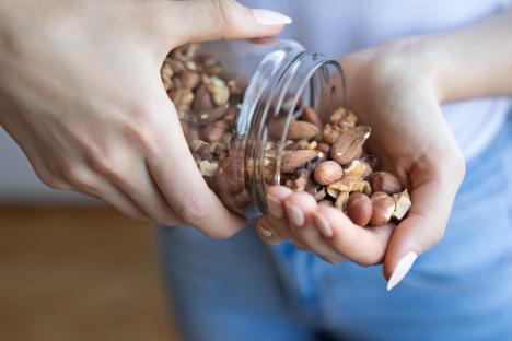 Hands pouring mixed nuts from a jar.
