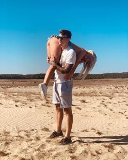Man carrying a woman on his back in a sandy landscape.