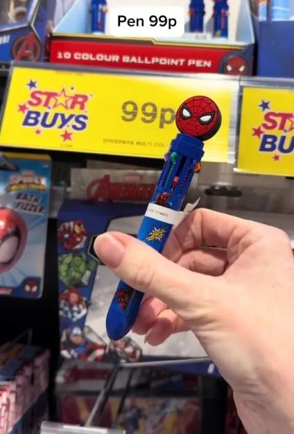 A hand holds a blue Spider-Man multi-color ballpoint pen, priced at 99p, in a store with other Marvel-themed items in the background.