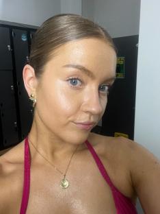 Woman with light makeup and hair pulled back, wearing a pink top and gold necklace.