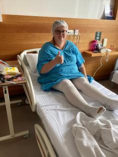 Woman in hospital bed giving thumbs up.