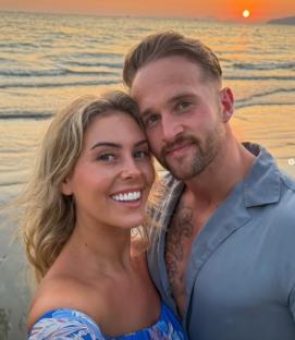 Couple posing for a selfie on a beach at sunset.