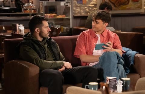 Two men sitting on a couch in a cafe, talking.