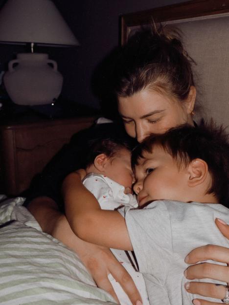 A mother cuddling her newborn baby and toddler.
