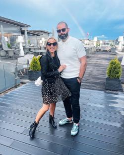 Couple posing on a rooftop terrace with a rainbow in the background.