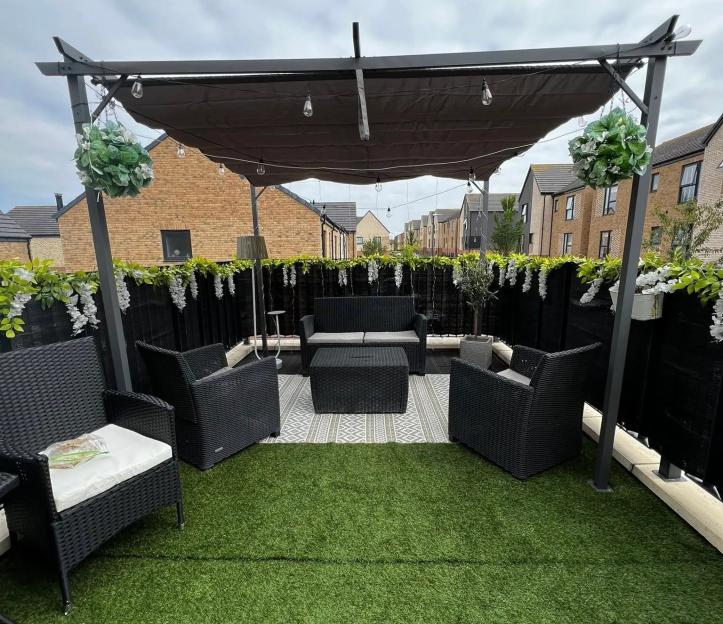 Small balcony transformed into an outdoor seating area with artificial grass, pergola, and hanging plants.