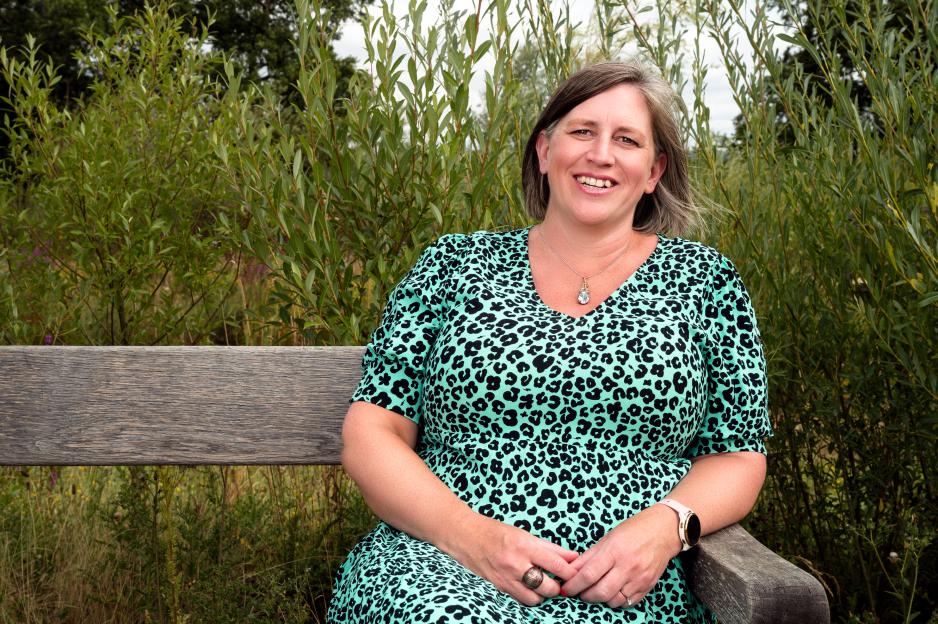 Woman in teal leopard print dress sitting on a bench outdoors.