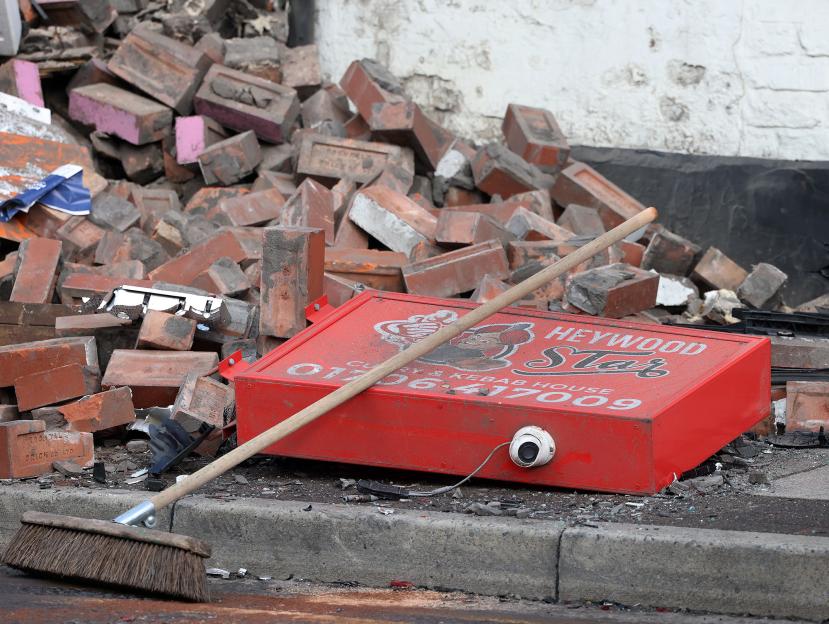 A red "Heywood Star Curry & Kebab House" sign, a broom, and scattered bricks on the ground after a car crash.