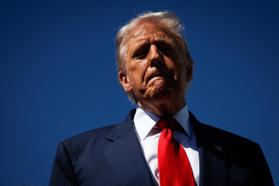 Donald Trump, in a dark suit and red tie, speaks to reporters at Palm Beach International Airport.
