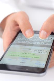 Close-up of hands using an iPhone to text on WhatsApp.