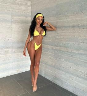 a woman in a yellow bikini is standing in front of a stone wall