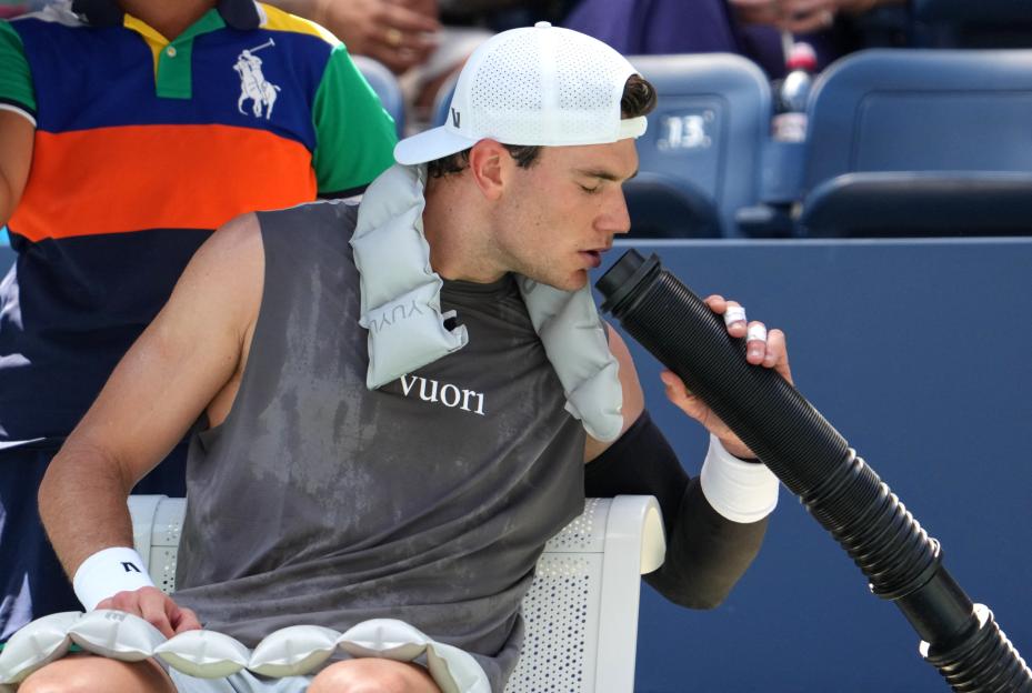 Sweaty tennis player Jack Draper drinks from a cooling device.