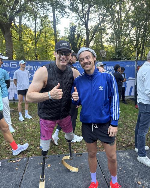 Harry Styles with an athlete who has prosthetic legs, both giving a thumbs-up.