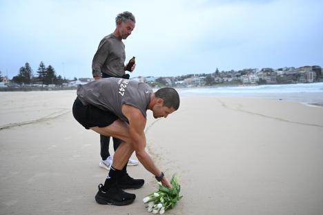 A man places lilies on the sand at Bondi Beach, his father watches.