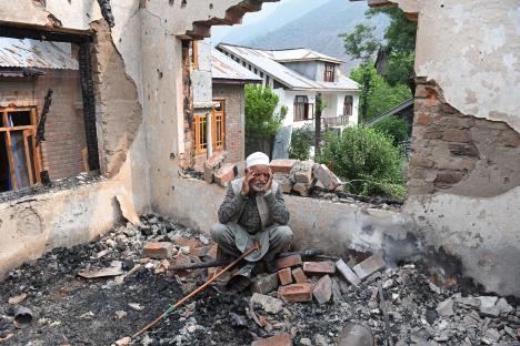 Elderly man sits amid the rubble of a destroyed house.