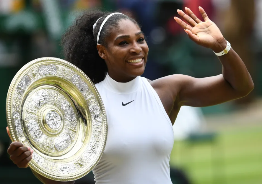 Serena Williams holding a trophy and waving.